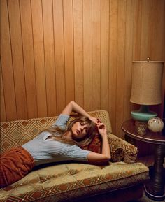 a woman laying on top of a couch next to a lamp