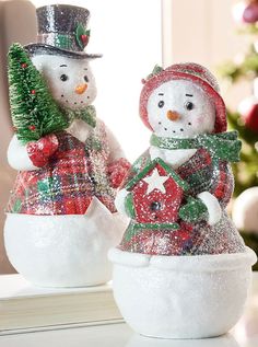 two snowmen are standing in an egg with a christmas tree on the other side