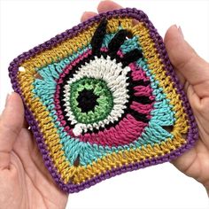 someone is holding up a crocheted square with an eye on the front and bottom