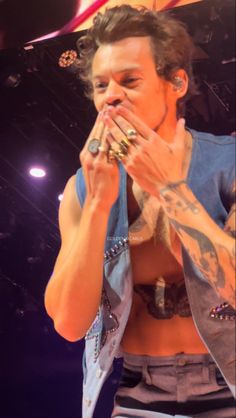 a man with tattoos on his chest and hands covering his mouth while standing in front of a stage