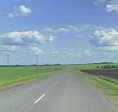 an empty road in the middle of a green field