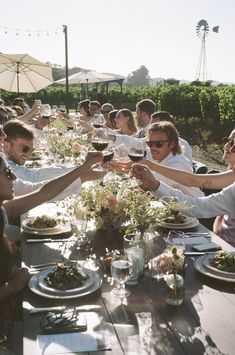 a group of people sitting at a table with wine glasses in their hands and plates full of food