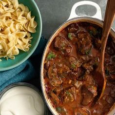 a pot filled with meat and vegetables next to two bowls full of pasta, cheese and sour cream