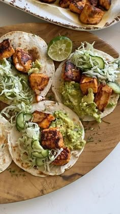 some tacos are sitting on a wooden platter with lime wedges and chicken