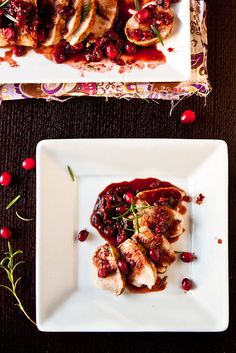 two white plates topped with meat covered in cranberry sauce and garnish