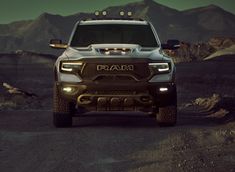 the front end of a silver ram truck on a dirt road with mountains in the background