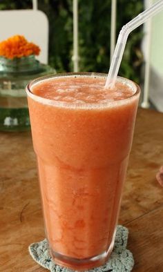 a smoothie with a straw in it sitting on a table next to an orange flower