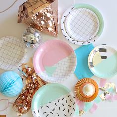 paper plates and decorations are arranged on a white tablecloth with gold, blue, and pink accents