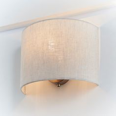 a wall light with a white fabric shade on the top and bottom half of it