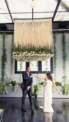 a bride and groom dancing under a chandelier with flowers hanging from the ceiling