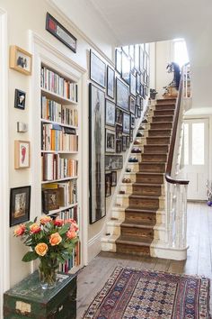 there is a stair case with many books on the wall and flowers in vase next to it