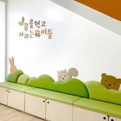 there is a green bench with stuffed animals on it in the room that has white walls and wood flooring