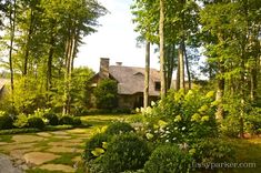 a house in the woods surrounded by lush green trees and bushes with stepping stones leading up to it