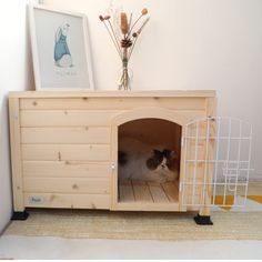 a cat sitting in a wooden dog house on top of a floor next to a wall