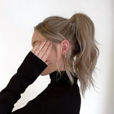 a woman covering her face with her hands while standing in front of a white wall