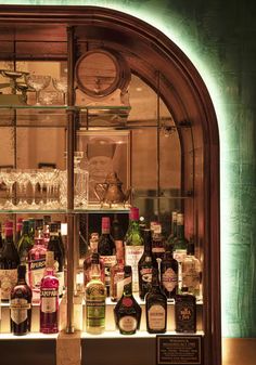 a display case filled with lots of different types of alcohol bottles and glasses in front of a clock