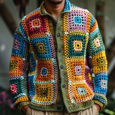 a man wearing a multicolored crocheted jacket and tan pants with his hands in his pockets