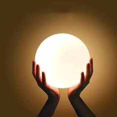 two hands are holding a glowing ball in the middle of their palms, against a brown background