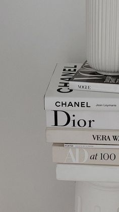 three books stacked on top of each other in front of a white vase and wall