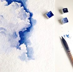 the watercolor is being used to paint clouds in blue and white colors on paper