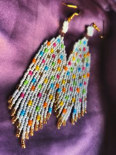 a pair of beaded earrings on top of a purple cloth