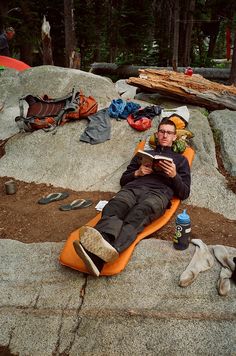 a man laying on top of a large rock next to a dog and camping gear