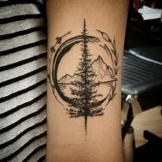 a tattoo on the arm of a person with a tree and mountains in the background