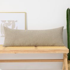 a pillow sitting on top of a wooden bench next to a green cactus in a white room