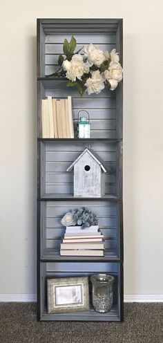 a book shelf with flowers and books on it in front of a wall mounted birdhouse