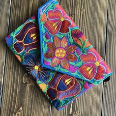 two colorfully embroidered clutches sitting on top of a wooden table