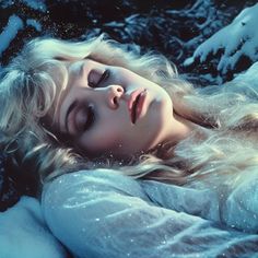 a woman laying down in the snow with her eyes closed and long hair blowing back