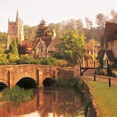 an old stone bridge over a river in the middle of a village with houses on either side