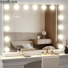 a white vanity with lights on it in front of a mirror and desk area next to a bed