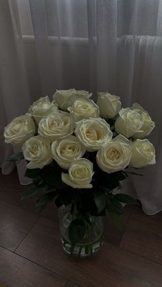 a vase filled with white roses sitting on top of a wooden floor next to a window