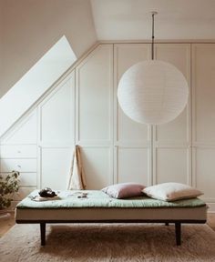 a bed sitting under a white light next to a wall mounted lamp on top of a wooden floor