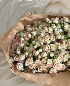 a bouquet of white and pink roses in a brown paper wrapper on a bed