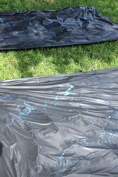 two black tarps covered in blue paint sitting on the grass