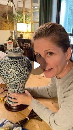 a woman holding up a vase on top of a wooden table