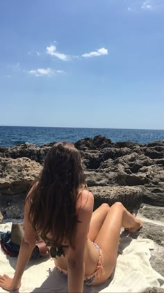 a woman sitting on top of a towel next to the ocean