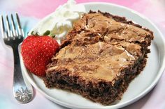 a white plate topped with brownies and whipped cream next to a strawberry on top of a table