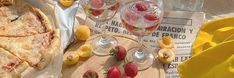 a table topped with pizza and fruit next to glasses filled with water, lemons and strawberries