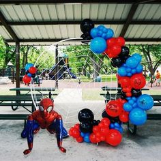 a spiderman balloon arch in the middle of a park with balloons attached to it