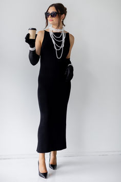 a woman in a black dress is holding a coffee cup and wearing pearls on her neck