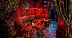 the interior of a restaurant with red lighting and colorful curtains on the walls, tables and stools