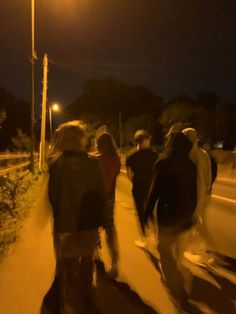 a group of people walking down a sidewalk at night