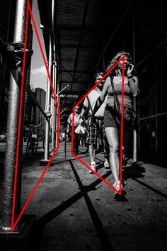 a woman walking down a street next to a tall pole with red lines on it