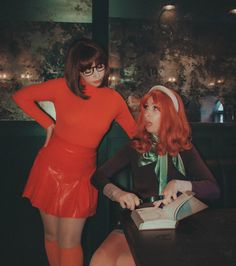 two women in red dresses are sitting at a table and one is reading a book