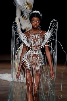 a model walks down the runway in a white dress with feathers on her head and body