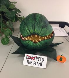 a fake dinosaur head sitting on top of a desk next to a sign that says don't feed the plant