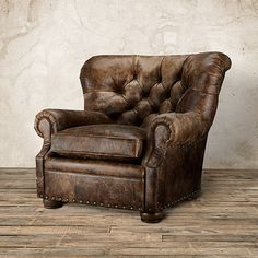 a brown leather chair sitting on top of a hard wood floor next to a wall